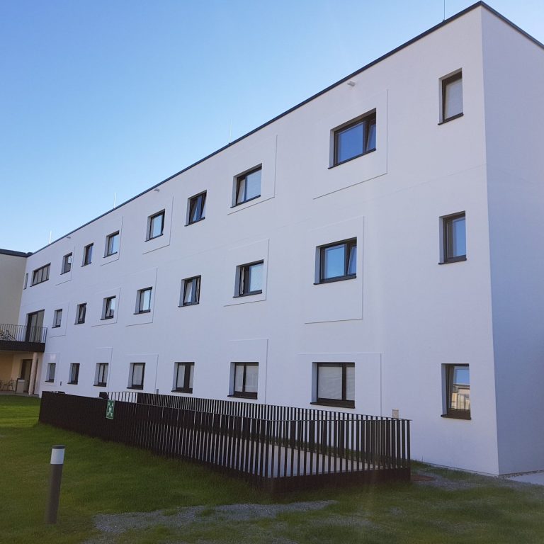 Modernes dreigeschossiges Gebäude mit neuer Fassadendämmung und Fenstern.